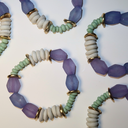 Three beaded bracelets with purple, green, and white beads on a light background